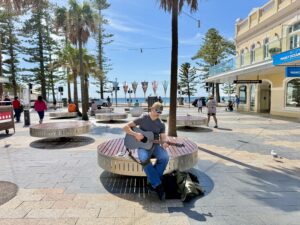 A man playing guitar on a boardwalk in front of a beach