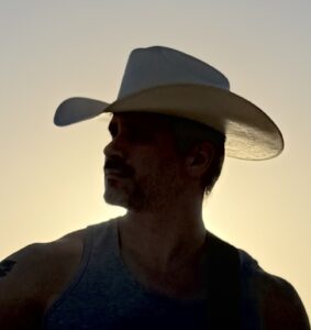 Silhouette of Patrick Kozub, a man, wearing a cowboy hat against a sunset